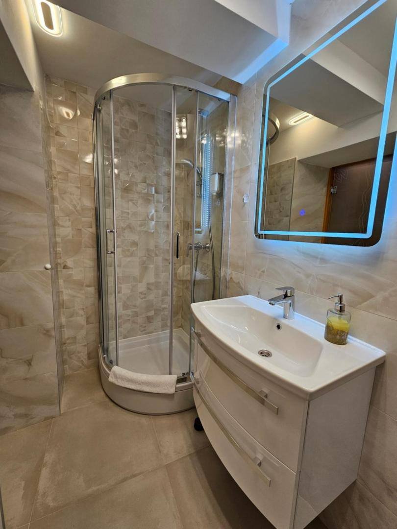Bathroom with a round glass shower, a vanity and a lit mirror